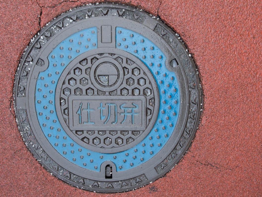 Decorative manhole cover with blue circle and pick background, Tokyo, Japan